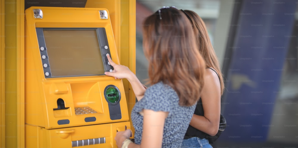 Duas belas fêmeas asiáticas retirando o dinheiro de um cartão bancário usando a máquina ATM no shopping