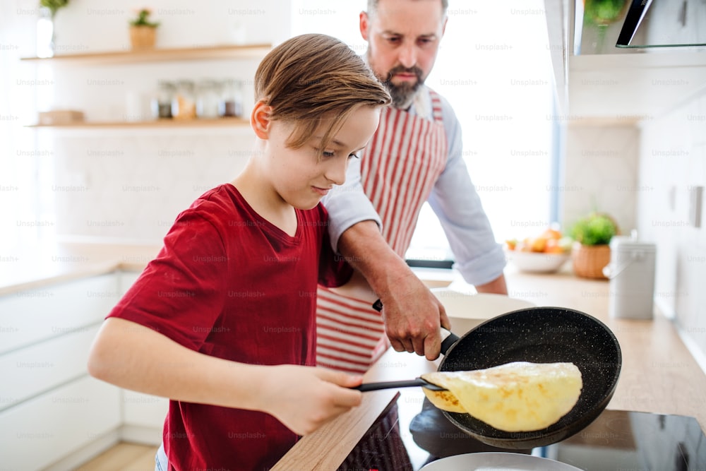 Um menino pequeno com pai dentro de casa na cozinha, aprendendo a fazer panquecas.