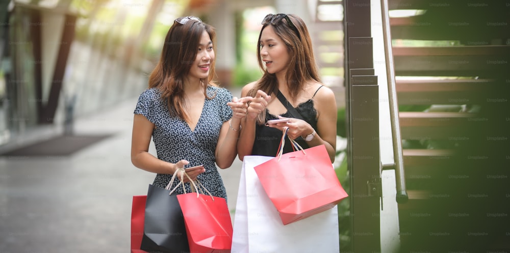 Mujeres asiáticas que pasan su tiempo libre comprando en el centro comercial y charlando juntas mientras sostienen la bolsa de compras