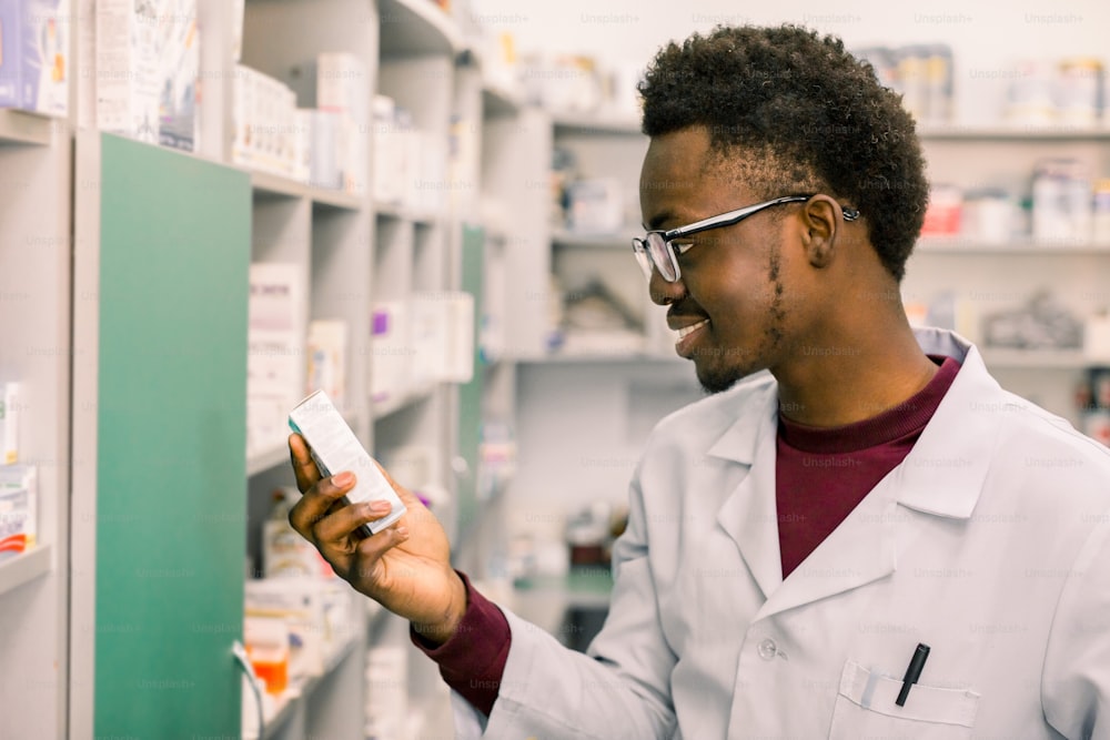 Close-up portrait of young African American man pharmacist searching prescribed drug on shelves in pharmacy.