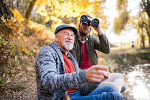 Senior father and his son with binoculars sitting on bench in nature, talking.