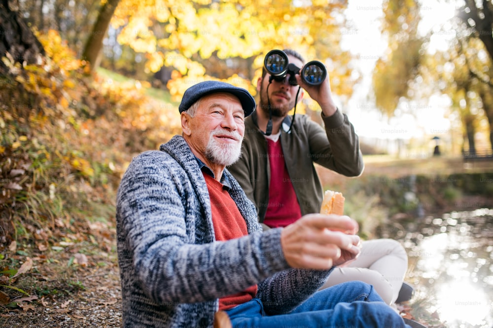 Padre anziano e suo figlio con binocolo seduti su una panchina nella natura, parlando.