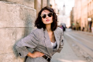Trendy fashion woman in jacket and sunglasses walking on the street, urban city scene. Copy space.