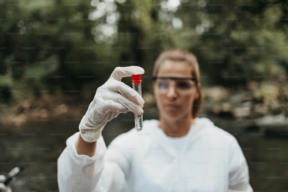 防護服を着た女性科学者、生物学者、研究者が汚染された川から水のサンプルを採取。