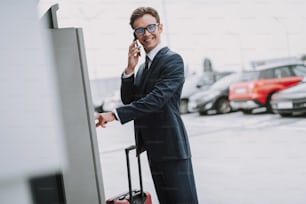 スーツケースを持った幸せなビジネスマンの腰を上げた肖像画がパーキングメーターの近くに立っていて、チェックを入れています。右側のスペースをコピー