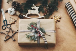 Elegante caja de regalo rústica de Navidad, papel de regalo, renos de madera, ramas y conos de pino, galletas de jengibre en mesa de madera rural. Feliz Navidad. Tarjeta de felicitación de las temporadas