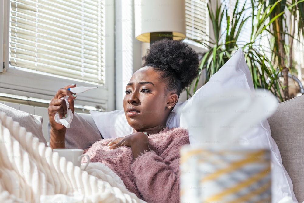 Enfermedad, concepto de problema de virus estacional. Mujer enferma que tiene gripe acostada en el sofá mirando la temperatura en el termómetro. Mujer enferma acostada en cama con fiebre alta. Resfriado, gripe y migraña.