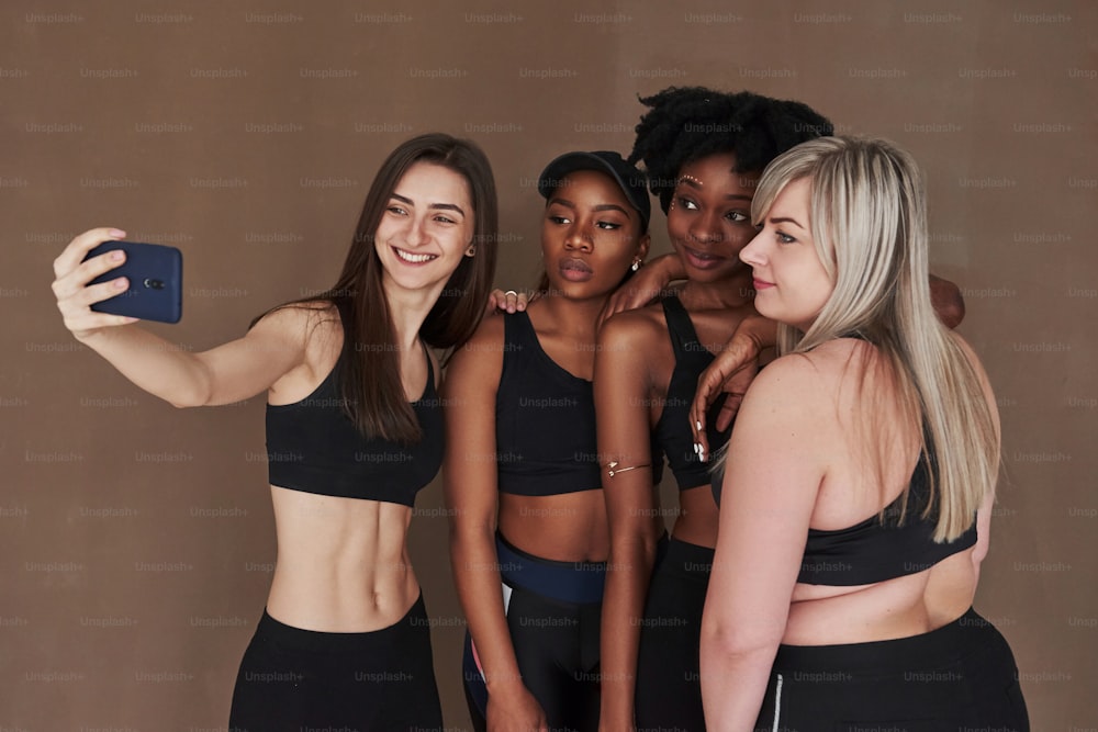 Selfie machen. Gruppe multiethnischer Frauen im Studio vor braunem Hintergrund.