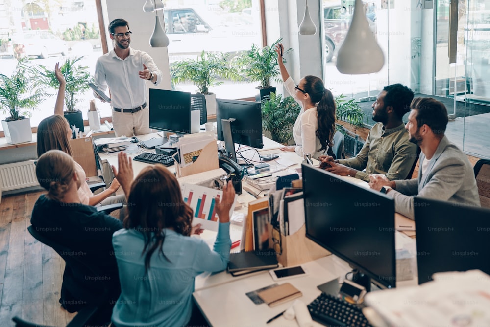 Group of young modern people in smart casual wear communicating and using modern technologies while working in the office