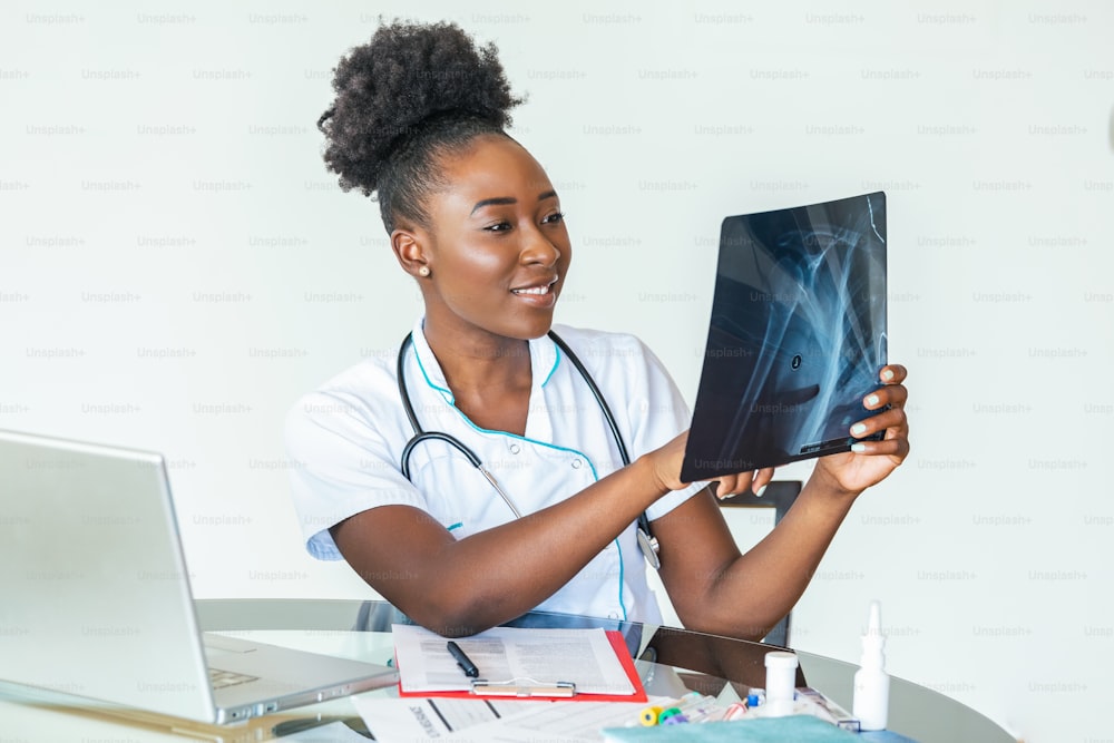 Woman doctor in hospital looking at x-ray film healthcare, roentgen, people and medicine concept. Young smiling female doctor with stethoscope pointing at X-ray at doctor's office