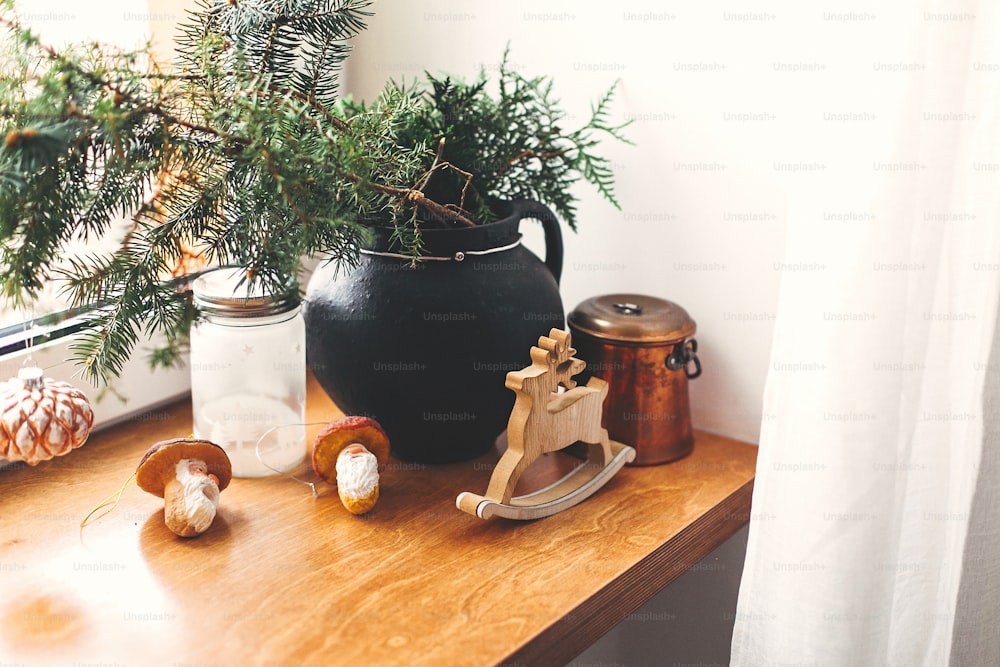 Stylish christmas decor on wooden windowsill. Pine branches with vintage bauble, wooden deer, lantern, mushroom toys on rustic windowsill. Cozy winter decoration