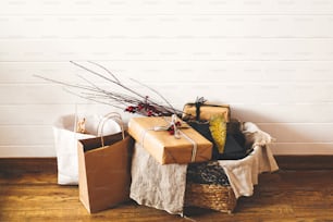 Stilvolle Weihnachtsgeschenkboxen auf Holzboden unter Weihnachtsbaum. Geschenke und Ornamente in rustikalen Körbchen und Papiertüten. Einkaufen im Urlaub. Verpackte Geschenke