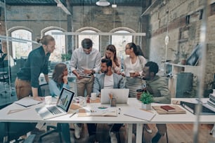 Group of young modern people in smart casual wear communicating and using modern technologies while working in the office