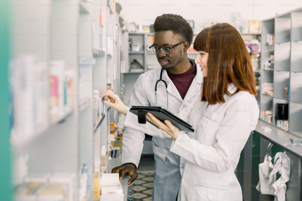 Confident Male And Female Pharmacists In Pharmacy. female pharmacist talking with her colleague about the attributes and side effects of a medicine or pharmaceutical product for sale, in the pharmacy.