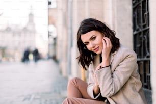 Street portrait of young beautiful happy smiling woman wearing stylish coat and pants. Model looking at camera. Female fashion concept. Copy space, free text.