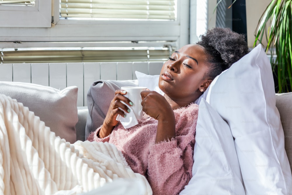 Cold And Flu. Portrait Of Ill African American Woman Caught Cold, Feeling Sick And Sneezing In Paper Wipe. Closeup Of Beautiful Unhealthy Girl Covered In Blanket drinking tea. Healthcare Concept.