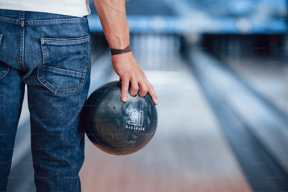 Artificial lighting. Rear particle view of man in casual clothes playing bowling in the club.