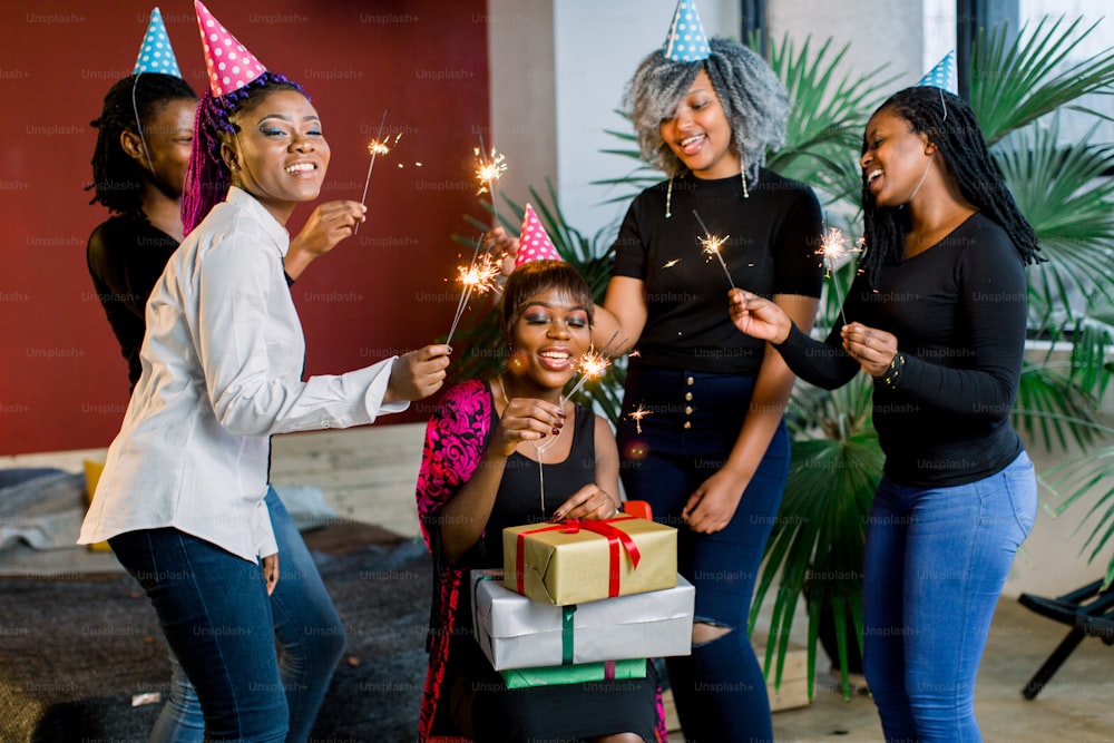 Afrikanische Freunde feiern Geburtstag und halten bengalische Lichter und mit Hüten und Geschenken