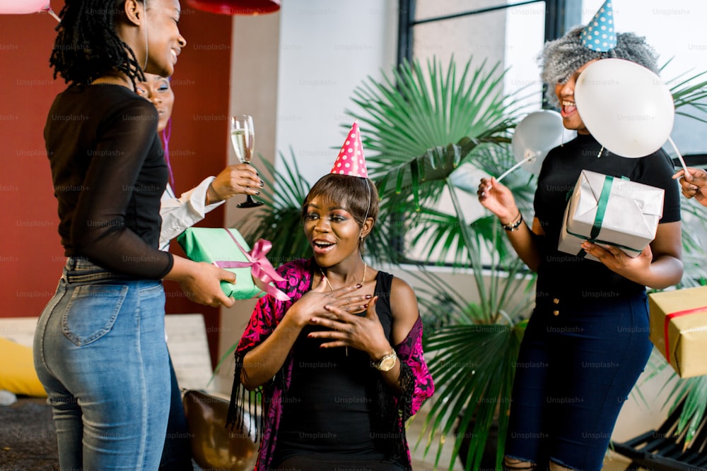 Jóvenes hermosas chicas afroamericanas con globos y sombreros celebran el cumpleaños y dan regalos de cumpleaños.