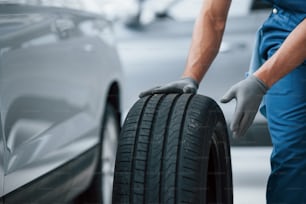 Customer will not wait. Mechanic holding a tire at the repair garage. Replacement of winter and summer tires.