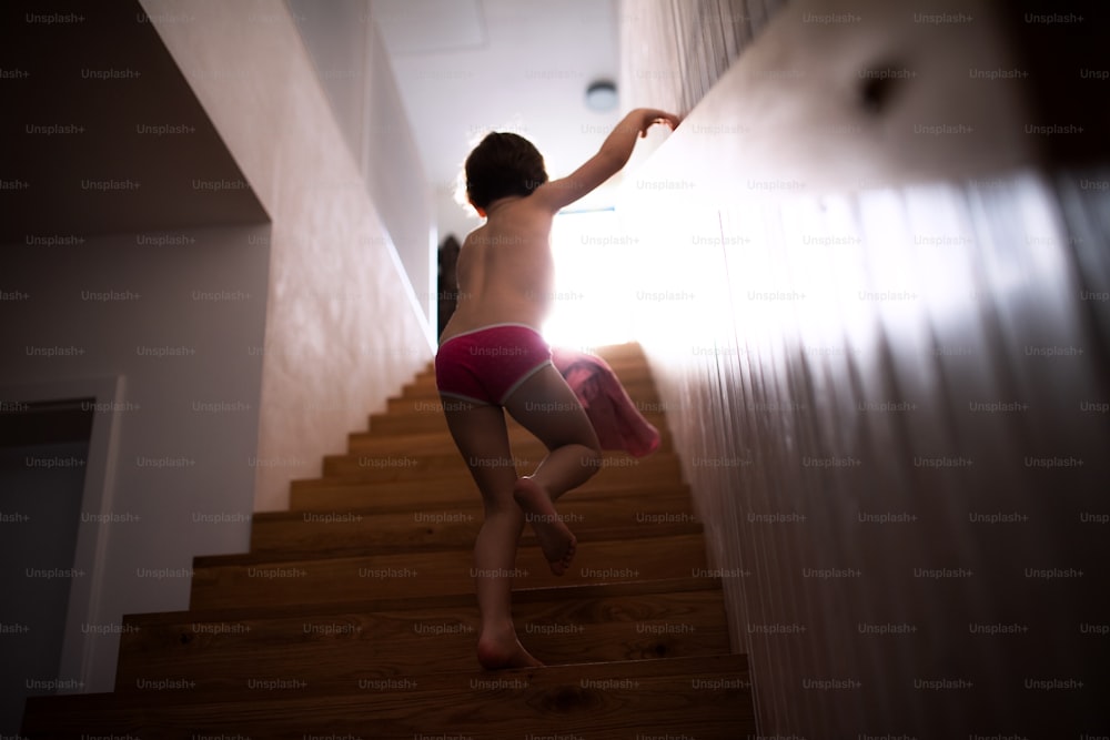A rear view of small child walking up the stairs, holding onto railing.