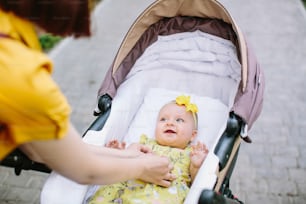 Pretty baby girl in yellow dress in stroller smiling to her mother