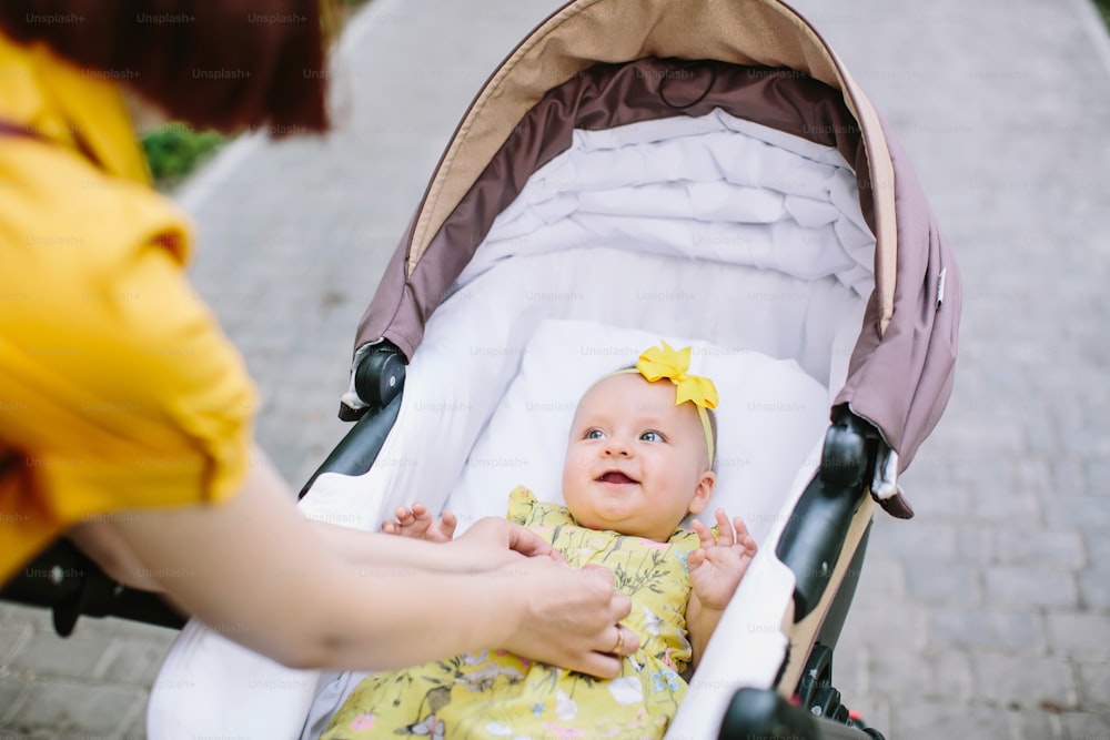 Pretty baby girl in yellow dress in stroller smiling to her mother