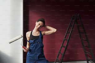 In the blue uniform. Young housewife decided to glue wallpaper in her new house in the room.