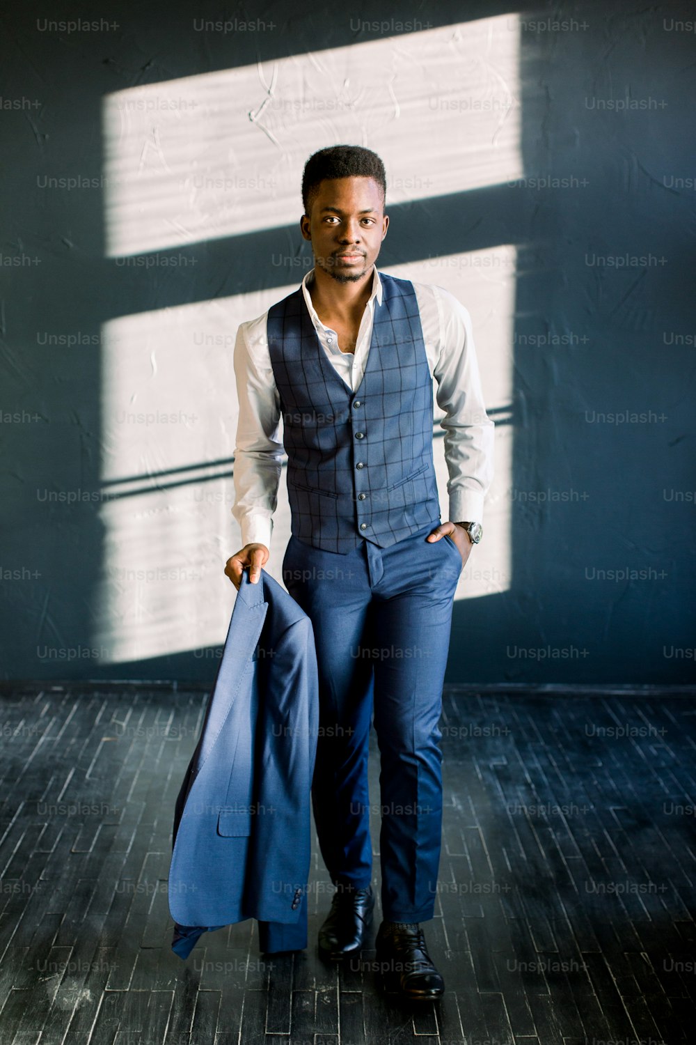Stilvoller afroamerikanischer Geschäftsmann mit einer Jacke in der Hand im modernen Büro