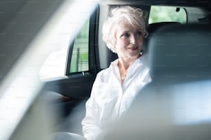Empresaria que viaja a la oficina en un lujoso automóvil sentada en el asiento trasero. Mujer de negocios senior en coche.