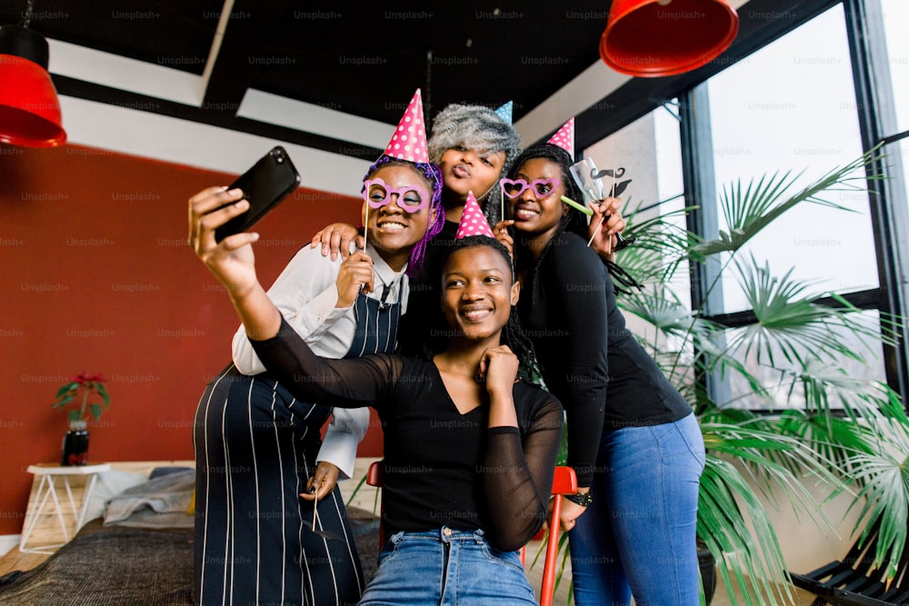 Glückliche afrikanische Mädchen feiern Geburtstag mit Hüten und fotografieren mit dem Smartphone