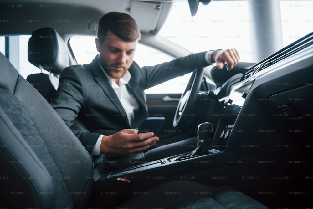 Time to stop and take a break. Modern businessman trying his new car in the automobile salon.