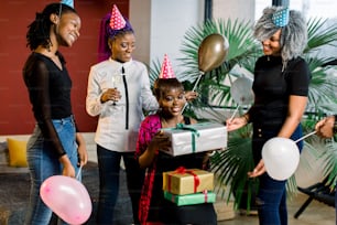 Young beautiful African American girls with balloons and hats celebrate birthday and give birthday gifts.