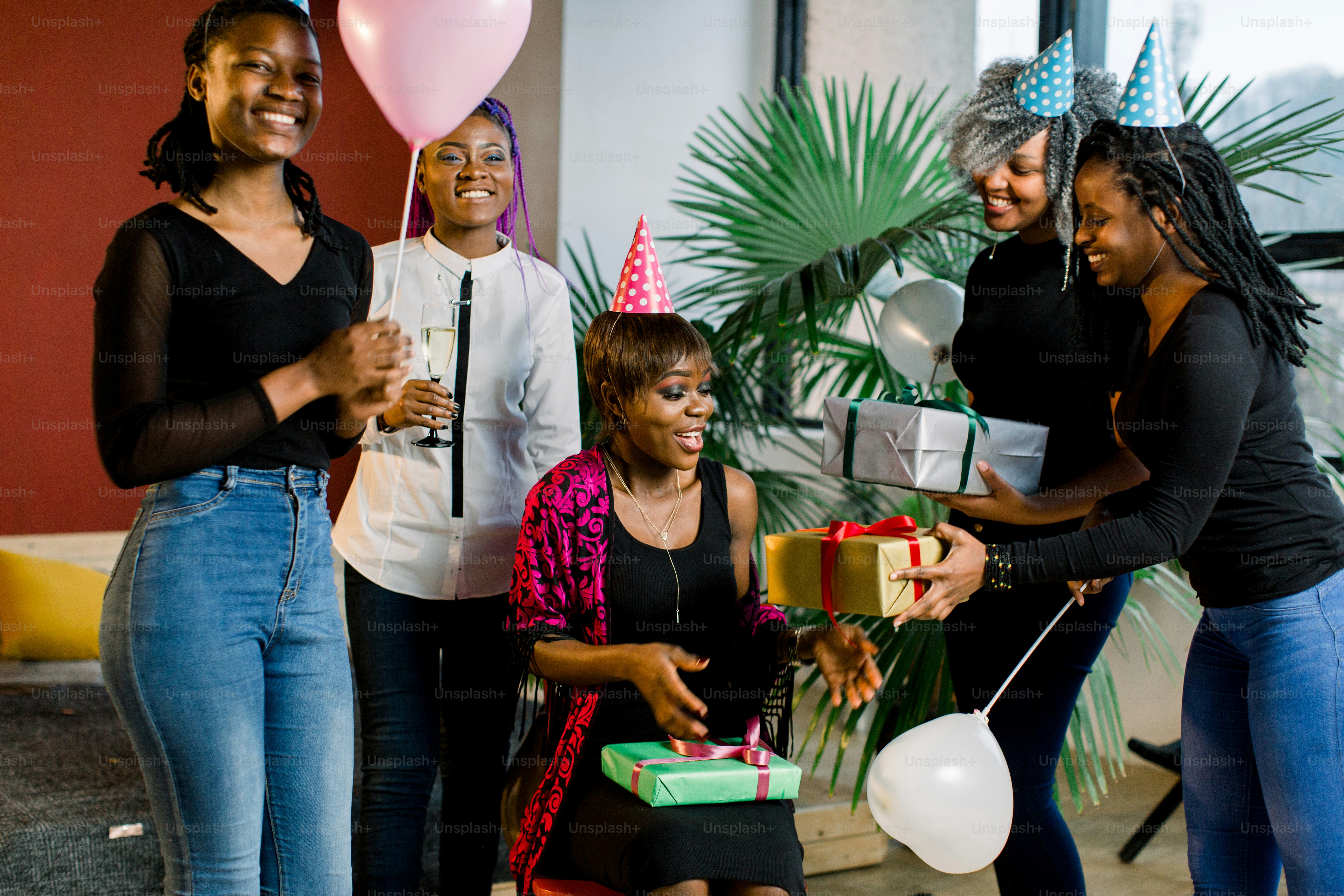 Gadis-gadis muda Afrika-Amerika cantik dengan balon dan topi merayakan ulang tahun dan memberikan hadiah ulang tahun.