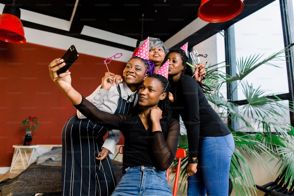 Des filles africaines heureuses célèbrent leur anniversaire avec des chapeaux et prennent des photos sur un smartphone