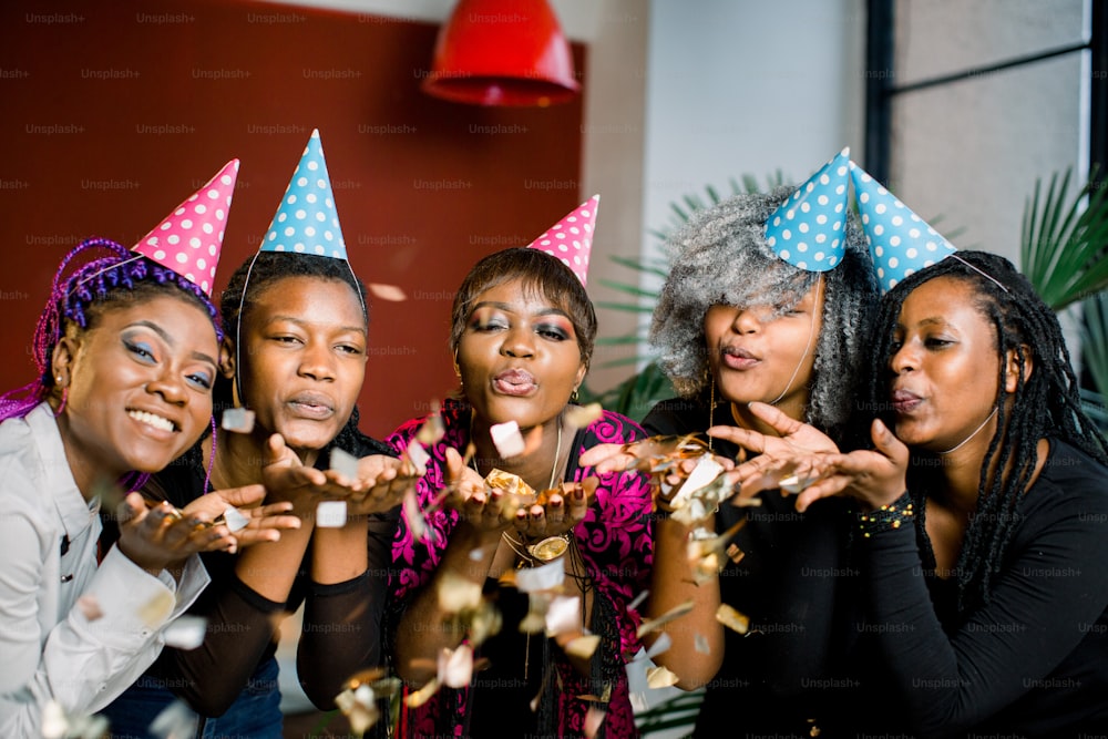 Konfetti-Party. Fröhliche junge afrikanische Gruppe von Menschen, die Silvester feiern und Konfetti blasen