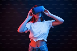Amazing modern technologies. Young woman using virtual reality glasses in the dark room with neon lighting.
