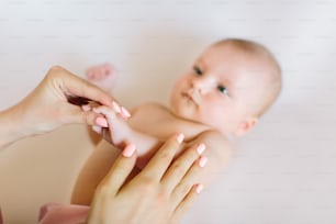 Main de mère massant l’avant-bras de son bébé sur fond blanc.