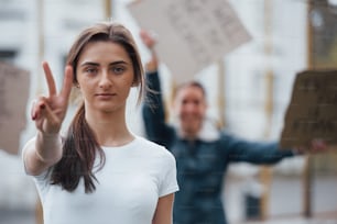 Deux doigts font un geste. Un groupe de femmes féministes manifestent pour leurs droits à l’extérieur.