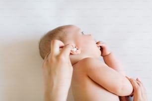 Mother hand cleaning baby ear with cotton swab.