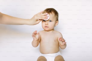 mother cleans face of a newborn baby girl whith a wadded disk isolated on white background. Hygiene, healthcare concept.