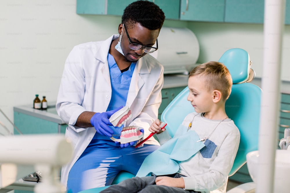 The child boy in dentist's chair having fun while brushing teeth with a male African American doctor