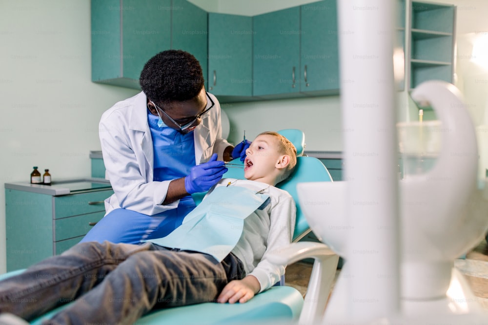Young beautiful boy in dental office. Children's African-American dentist examines teeth to a child.