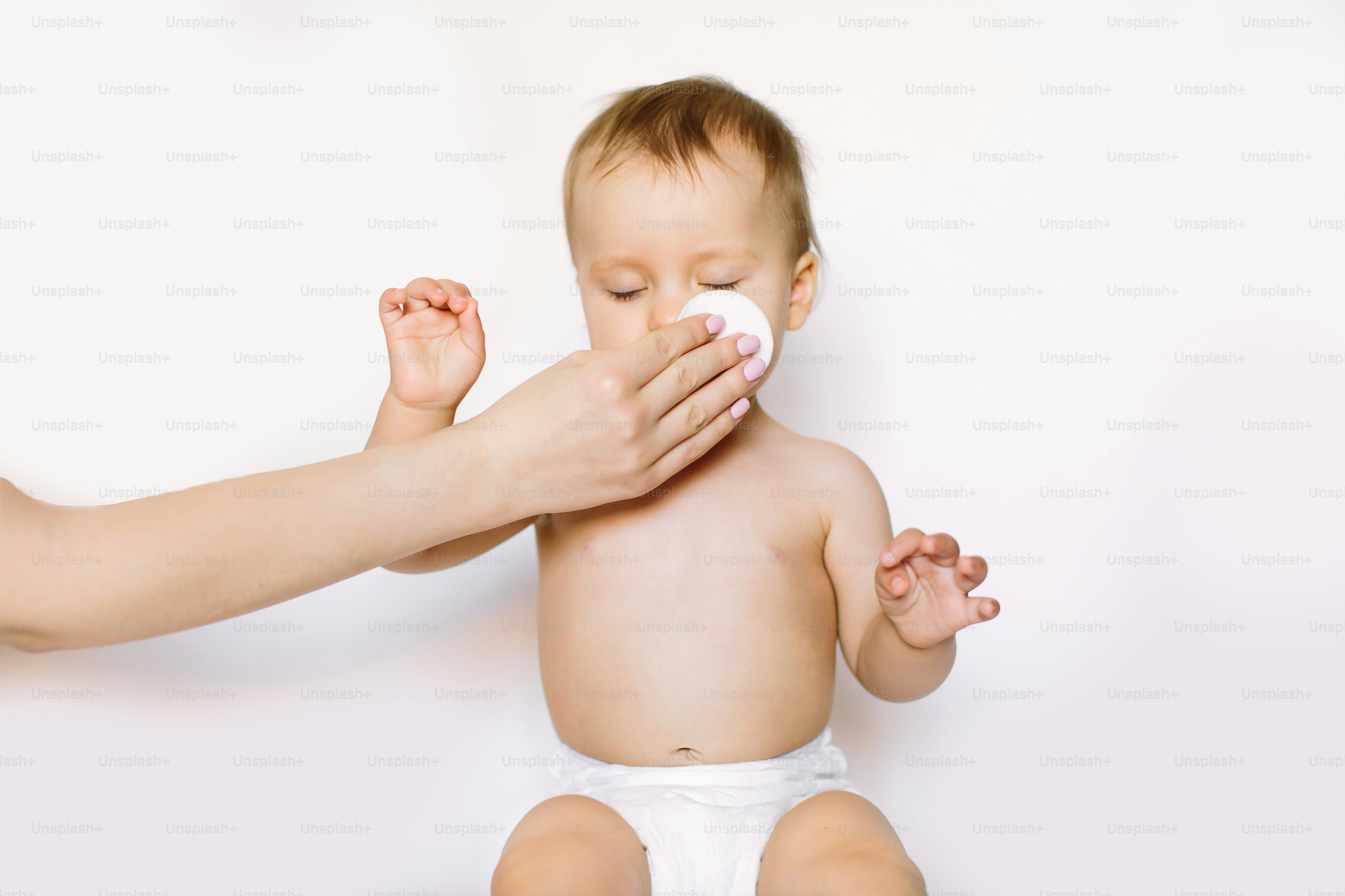 Mother cleaning eyes of a newborn baby with physiological solution on a cotton disk.