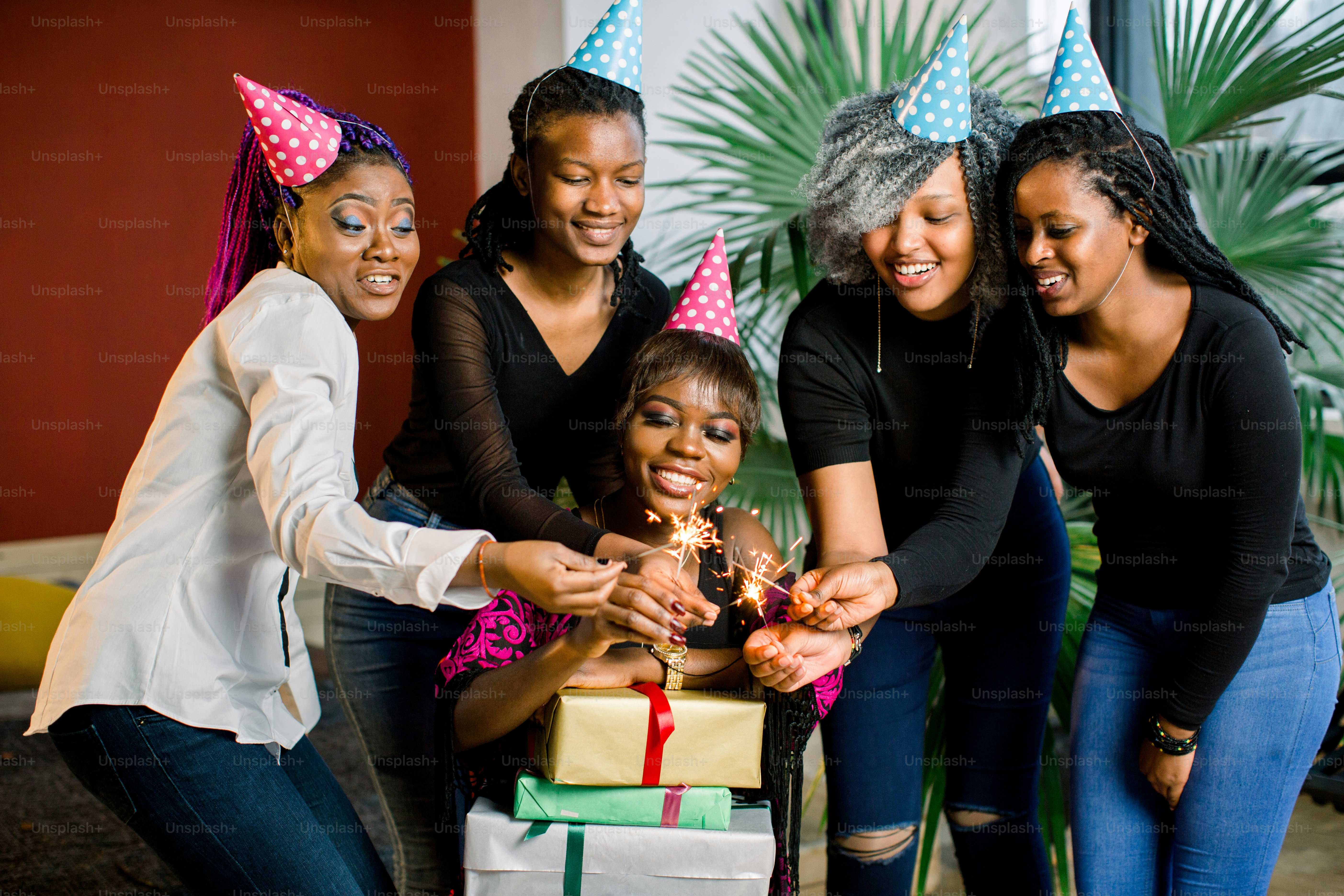 Seorang gadis Afrika yang cantik dan tersenyum memegang hadiah di tangannya dan merayakan ulang tahun bersama teman-temannya. Gadis-gadis memegang lampu bengal di tangan mereka