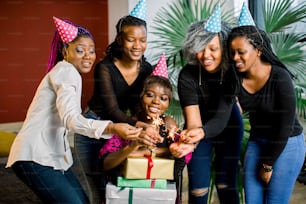 Una hermosa y sonriente niña africana sostiene regalos en sus manos y celebra su cumpleaños con amigos. Chicas sostienen luces de bengala en sus manos