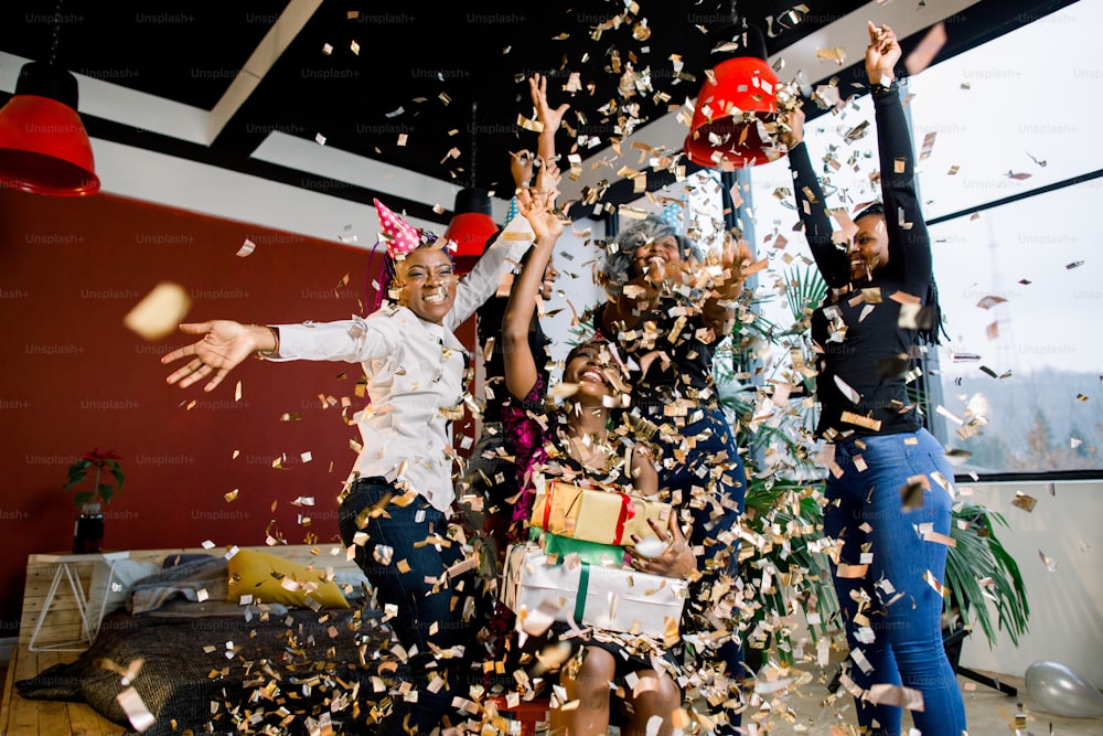 Happy African American friends girls under falling confetti at the birthday party