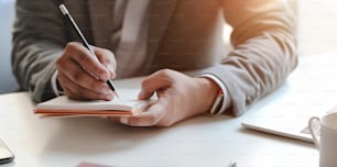 Close-up view of young professional businessman writing his idea concepts on notebook while working on his project