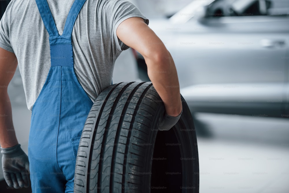 Repair concept. Mechanic holding a tire at the repair garage. Replacement of winter and summer tires.