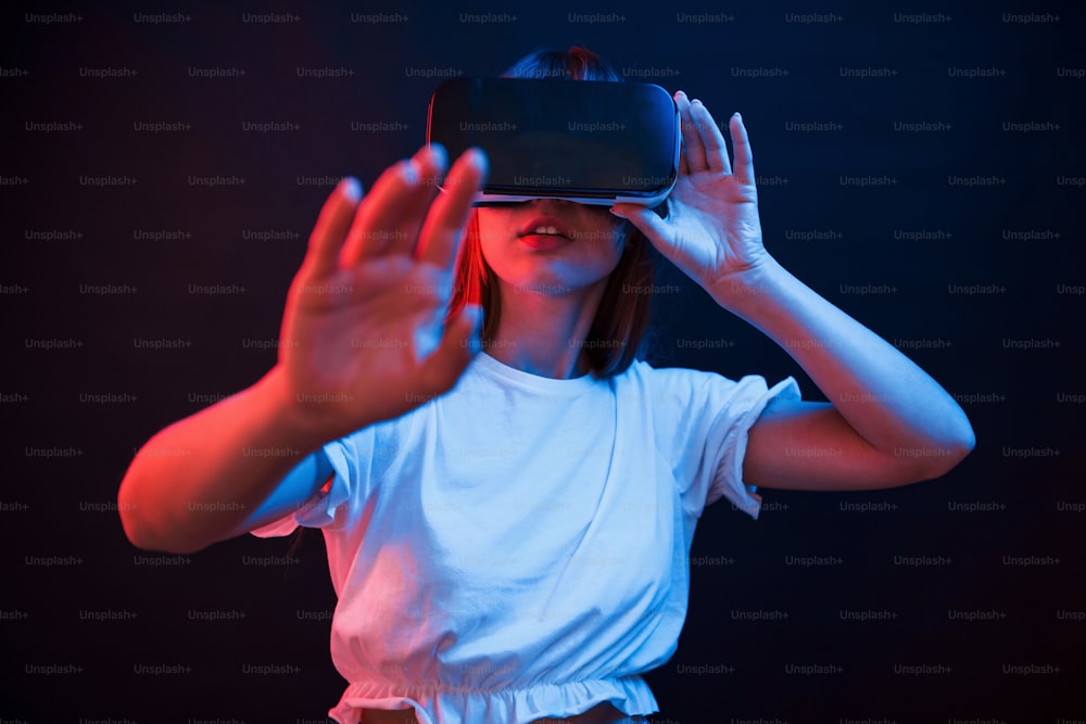 Tecnologie wireless. Giovane donna che utilizza occhiali per realtà virtuale nella stanza buia con illuminazione al neon.